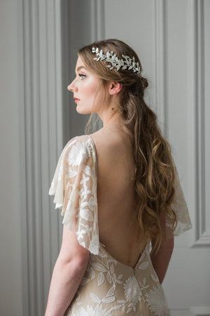 Model in white gown wearing a silver laurel leaf bridal heapiece wrapped around back of head