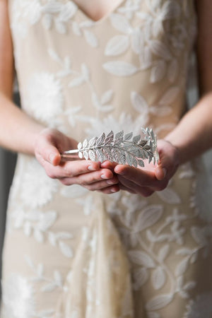 Model holding a bridal headpiece made of silver leaves