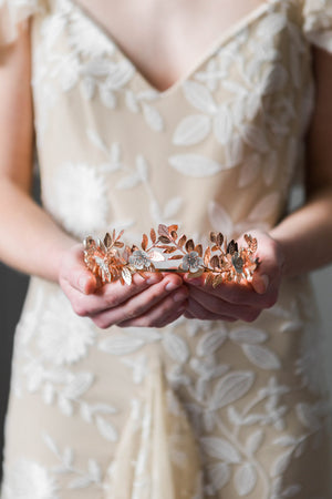 A bride holding a rose gold laurel leaf flower crown