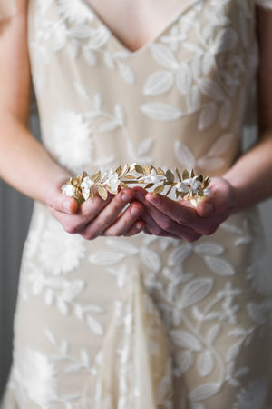 Bride holding a crown heapiece made of gold leaves and silk flowers