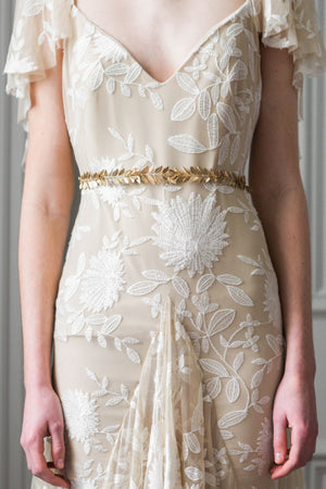 Model in a wedding dress wearing a gold leaf sash