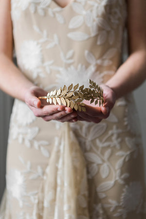 Model holding a bridal headpiece made of gold leaves