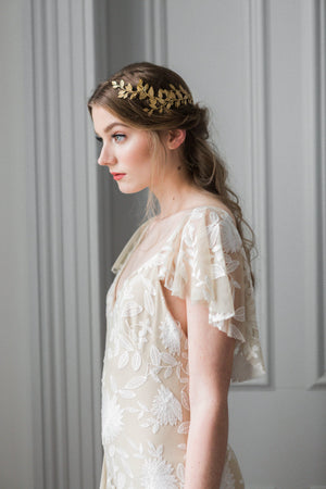 Model in white gown wearing a gold laurel leaf bridal heapiece wrapped around back of head